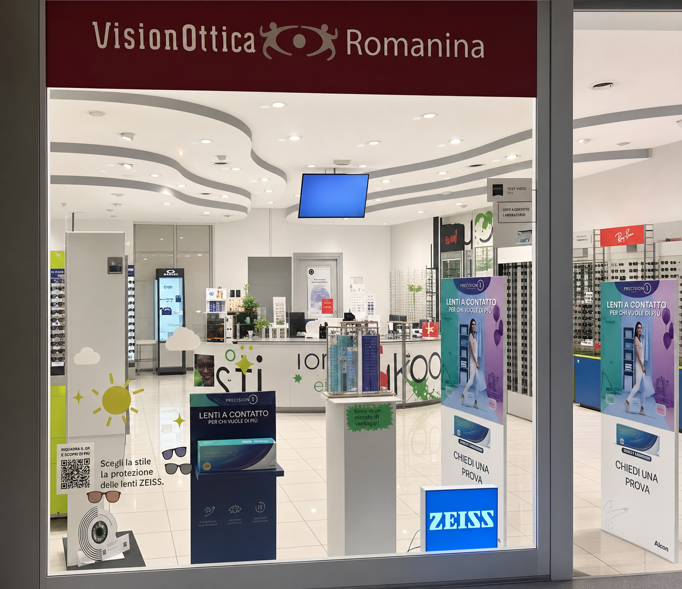 Ingresso del negozio VisionOttica Romanina di Roma in centro commerciale con insegna bordeaux, roll-up promozionali Zeiss all'interno, espositori di montature e totem laterali