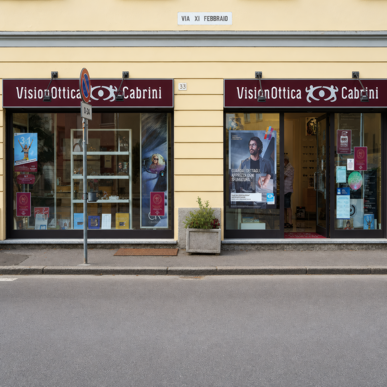 Facciata del negozio VisionOttica Cabrini di Soresina su strada con doppia insegna bordeaux, due vetrine con poster e montature esposte e targa stradale Via XI Febbraio