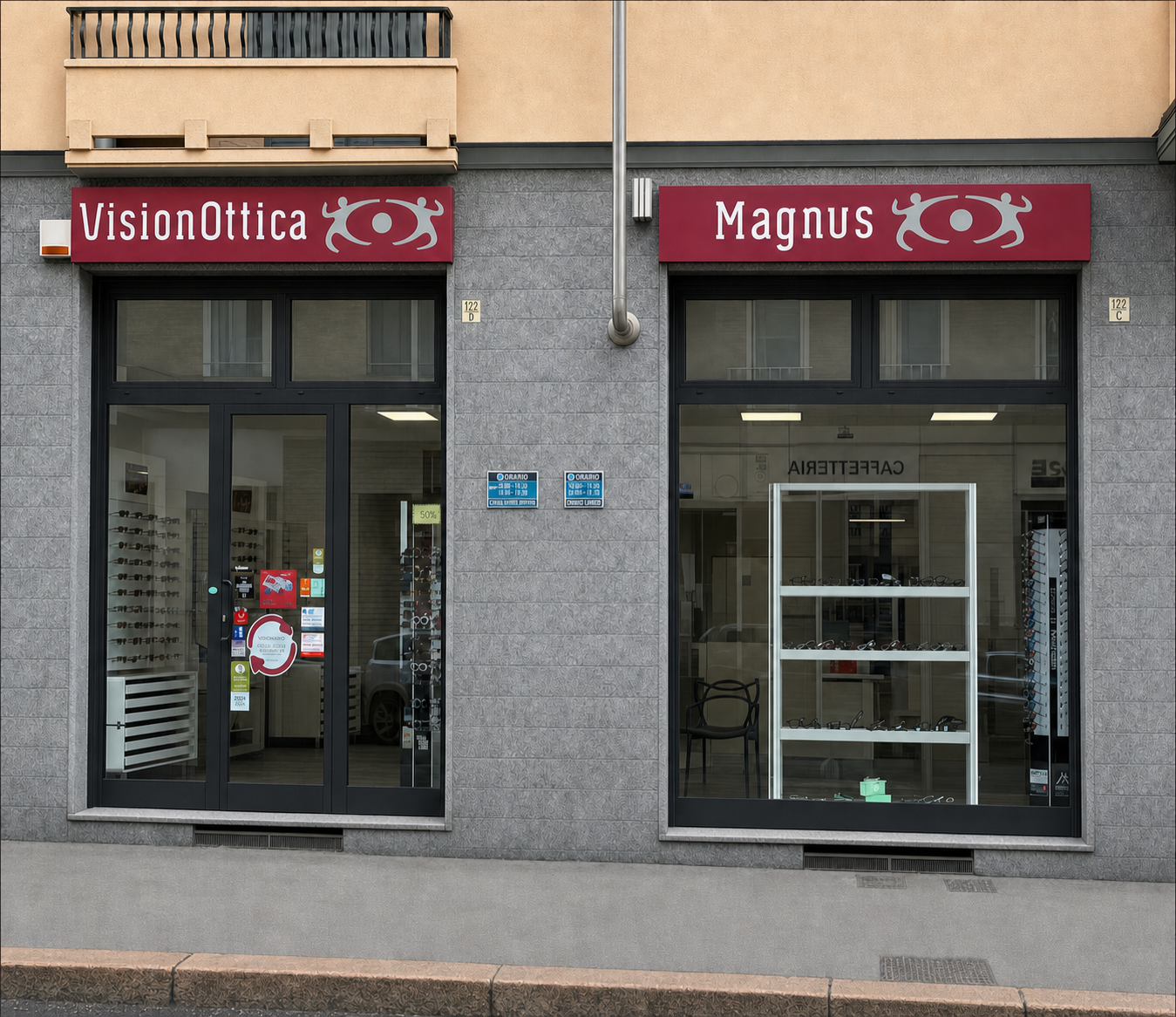 Facciata del negozio VisionOttica Magnus di Torino su strada con doppia insegna bordeaux separata, due vetrine su edificio in cemento grigio e caffetteria adiacente visibile